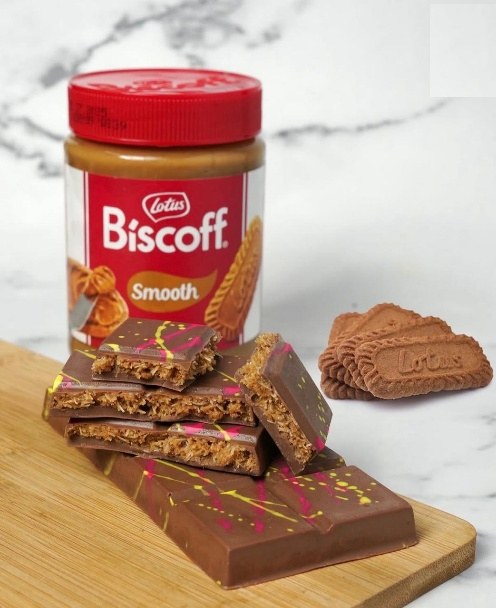 A Biscoff chocolate bar cut to show the layers, beside a jar of Biscoff spread
