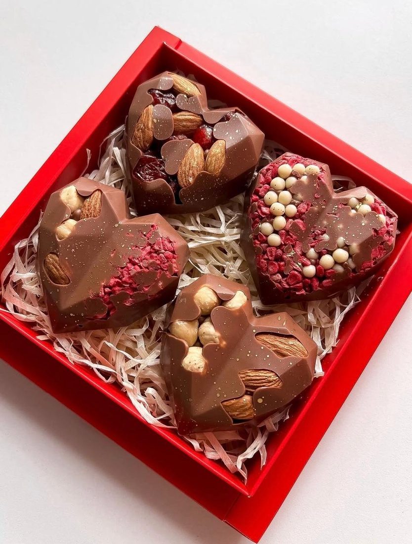 A red gift box holding four Meltova Big Bites, faceted hearts topped with whole almonds, cashew and freeze dried fruit
